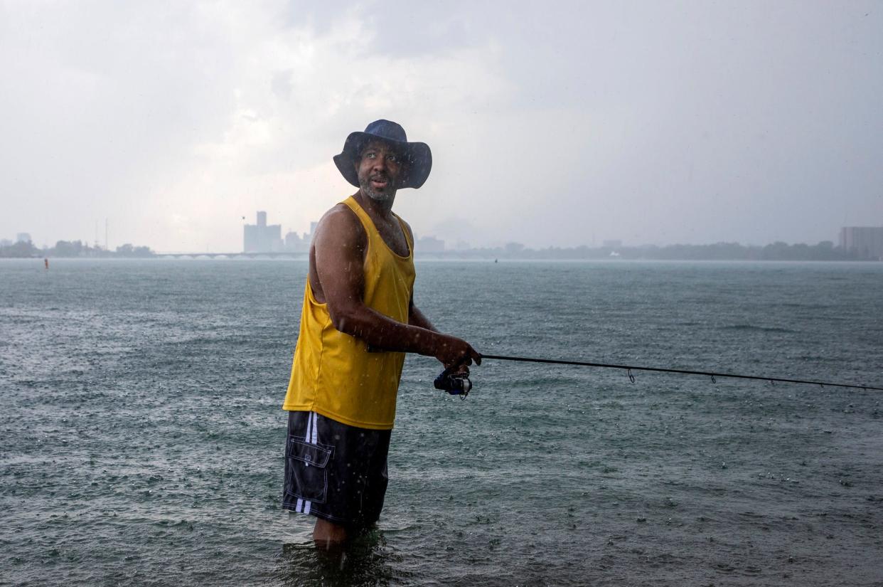 Jason Braxton, 47, of Detroit, looks over his shoulder at people passing by as he fishes on a Belle Isle beach while rain pours down on a hot Thursday afternoon in Detroit on Thursday, June 20, 2024.