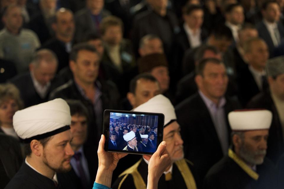 A Crimean Tatar's woman films as Russia's top Muslim Cleric Ravil Gainutdin, foreground center, deputy chairman of Russia Muftis Council Rushan hazrat Abbyasov, foreground left, and Mufti of Crimean Muslims Emirali Ablayev, foreground right, attend the Qurultay, a religious congress, in Bakhchysarai, Crimea, Saturday, March 29, 2014. The Crimean Tatar Qurultay, a religious congress will determine whether the Tatars will accept Russian citizenship and the political system that comes with it, or remain Ukrainian citizens on Russian soil. (AP Photo/Pavel Golovkin)