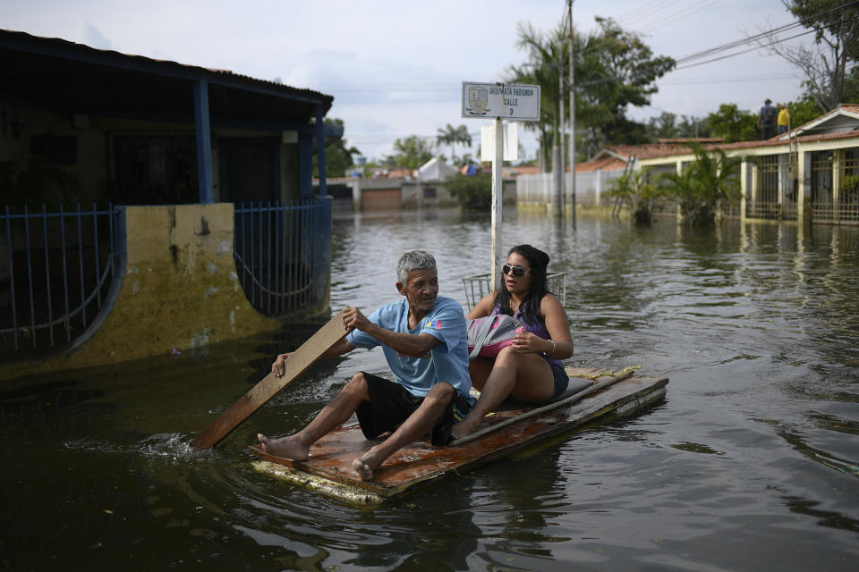 En esta imagen, tomada el 21 de octubre de 2020, un hombre utiliza una puerta a modo de balsa improvisada para trasladar a una mujer por las calles anegadas del vecindario de Mata Redonda, en Maracay, Venezuela. Las fuertes lluvias caídas en el estado de Aragua, en el centro de Venezuela, provocaron el desbordamiento del Río Madre Vieja inundando varios vecindarios. (AP Foto/Matías Delacroix)