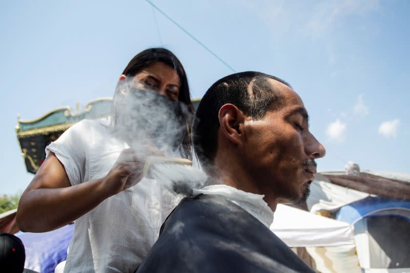 Un migrante solicitante de asilo, que fue aprehendido y devuelto a México bajo el Título 42 por cruzar la frontera de México a Estados Unidos, recibe un corte de pelo de un voluntario en una plaza pública donde cientos de migrantes viven en tiendas de campaña, en Reynosa, México