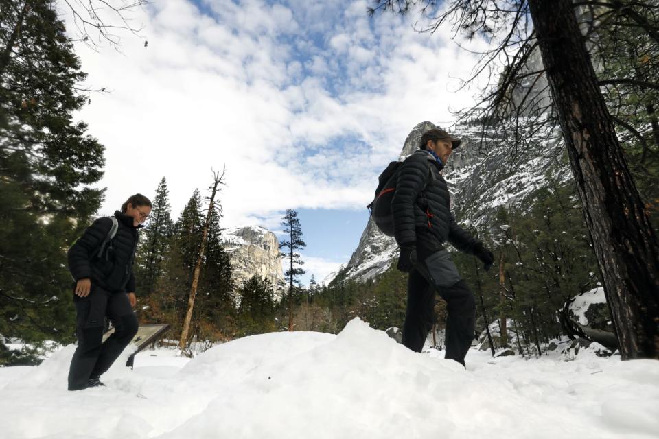 Two people walk through deep snow in the park.