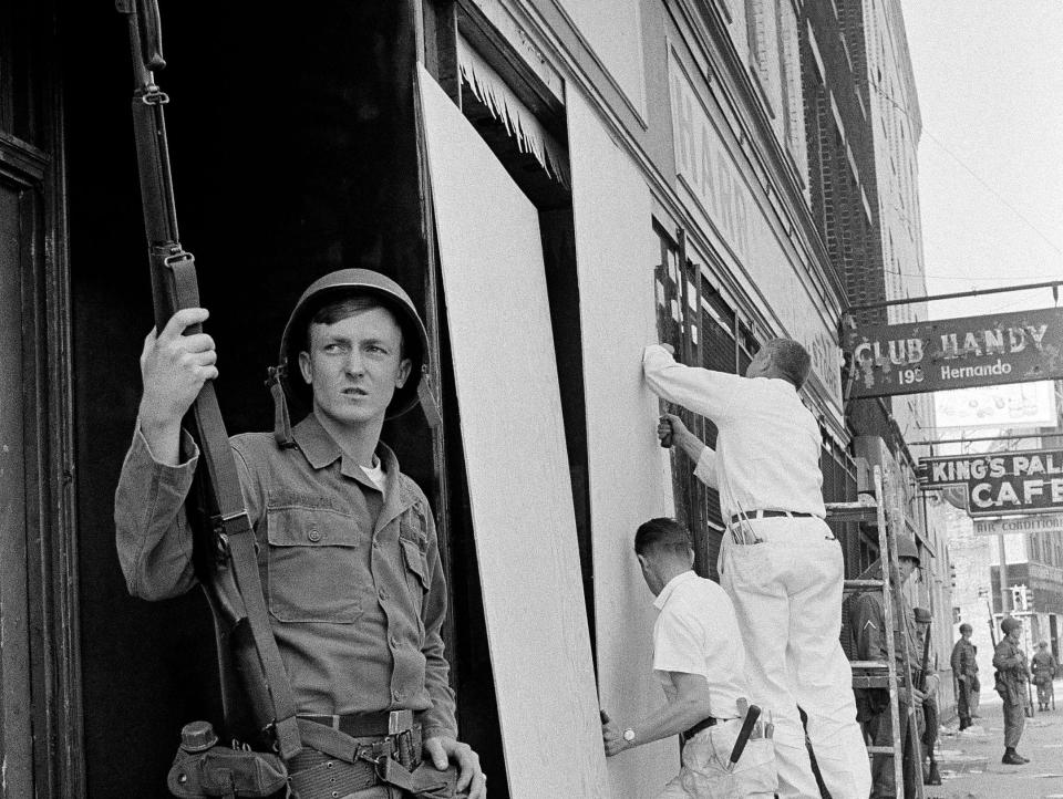 A National Guardsman with a bayoneted rifle stands guard in a doorway near the corner of Beale and Hernando Streets in downtown Memphis, Tenn., as workmen continue to board up store fronts in the wake of rioting and looting in the area, March 29, 1968.