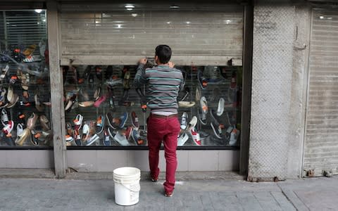 A worker closes the security shutter of a window display at a shoes store in downtown Caracas, - Credit: REUTERS/Marco Bello