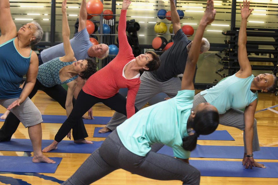 A group of seven people in a yoga class performing a side stretch pose on yoga mats in a gym