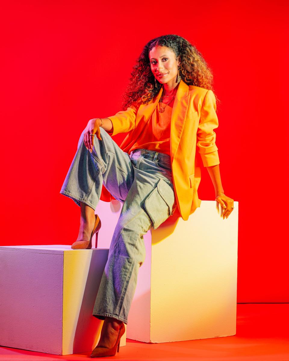 Elaine Welteroth in orange blazer, jean cargo pants and heels against a bright red background