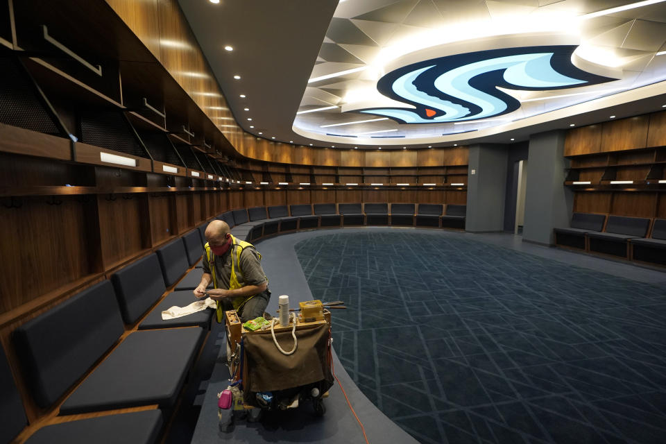 A worker puts the final touches on woodwork in the Seattle Kraken's locker room at Climate Pledge Arena, Wednesday, Oct. 20, 2021, during a media tour ahead of the NHL hockey team's home opener Saturday against the Vancouver Canucks in Seattle. The historic angled roof of the former KeyArena was preserved, but everything else inside the venue, which will also host concerts and be the home of the WNBA Seattle Storm basketball team, is brand new. (AP Photo/Ted S. Warren)