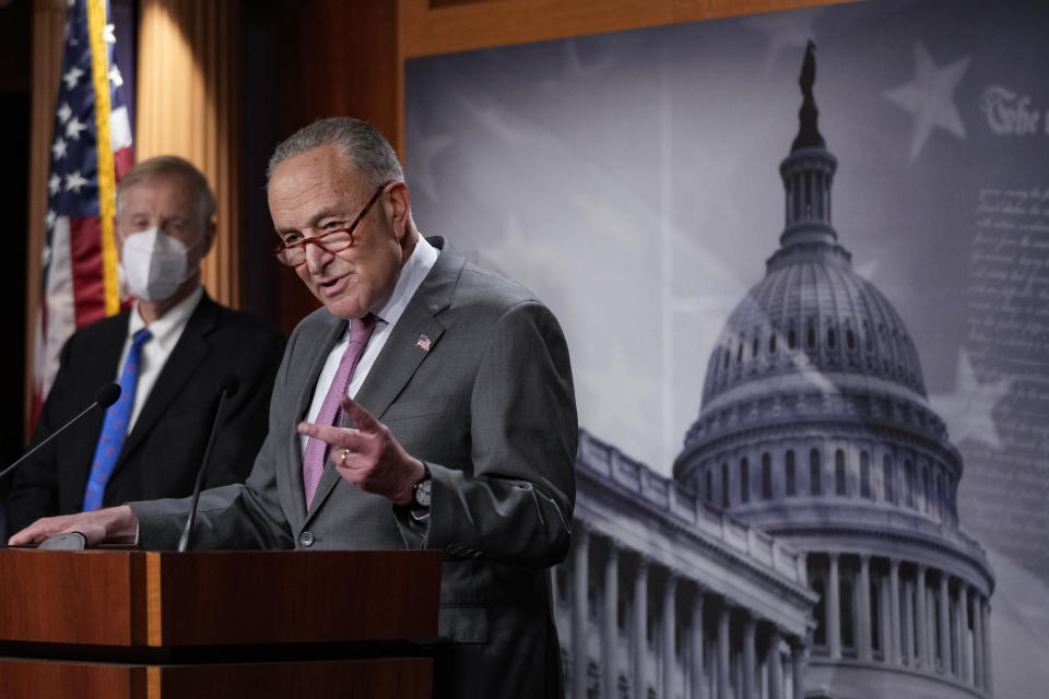 Senate Majority Leader Chuck Schumer stands at a podium in front of a photo of the U.S. Capitol. 