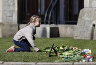 A young girl lays flowers as a tribute to Britain's Prince Philip outside Windsor Castle, Windsor, England, Tuesday, April 13, 2021. Britain's Prince Philip, husband of Queen Elizabeth II, died Friday April 9 aged 99. His funeral service will take place on Saturday at Windsor Castle. (AP Photo/Alastair Grant)