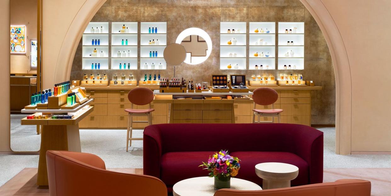 store interior with a large pink arch with glass cases and wooden drawers behind it and in the foreground is an intimate seating area with red and orangy pink velvet upholstered rounded sofa and rounded low armchairs