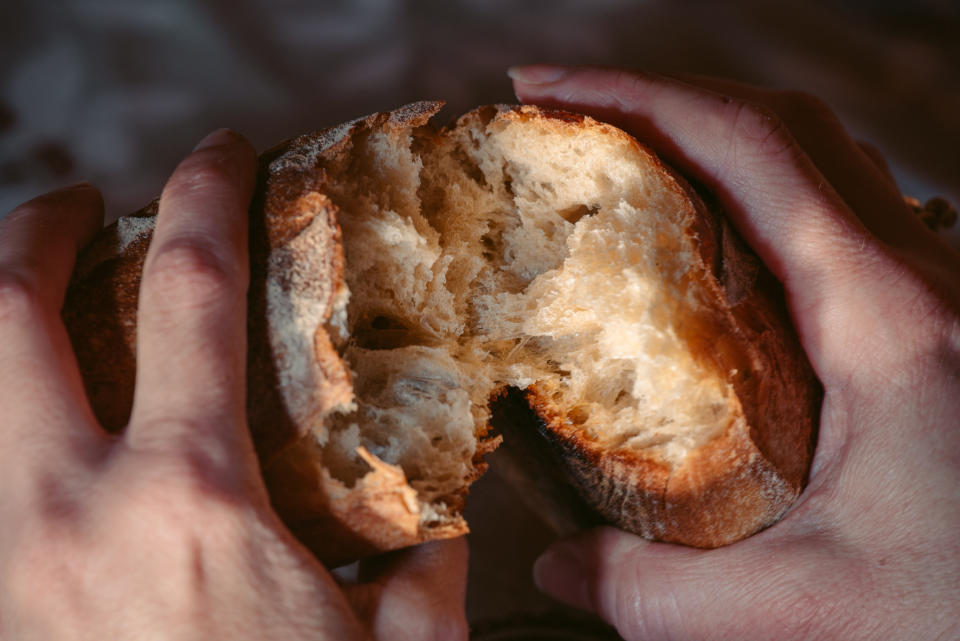 Hands tearing apart fresh baguette.