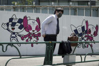 A man wearing a protective mask to help curb the spread of the coronavirus stands near drawings of Miraitowa and Someity, official mascots for the Tokyo 2020 Olympics and Paralympics, on a construction wall Tuesday, April 20, 2021, in Tokyo. (AP Photo/Eugene Hoshiko)