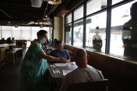 Highway Inn restaurant hostess Ku'uipo Lorenzo, left, seats two customers after they showed proof of vaccination on Monday, Oct. 25, 2021, in Honolulu. To comply with local mandates, the restaurant requires all indoor diners to show proof of vaccination or have a recent negative test result before being seated. (AP Photo/Caleb Jones)