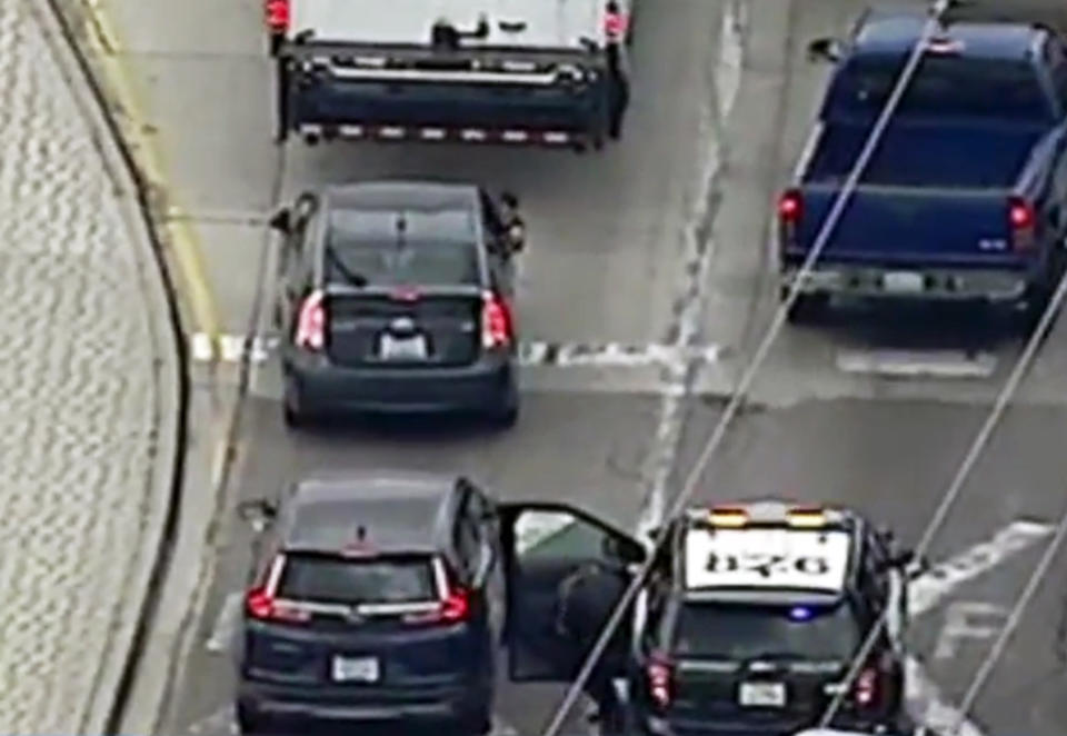 This photo taken from video provided by KABC-TV shows a man leaning out the passenger-side window of a car at top left, shooting at pursuing police vehicles as officers take cover, during a wild car chase in the Los Angeles area Friday afternoon, May 10, 2019. The car finally came to a halt in the Los Angeles suburb of Vernon, where the woman driver, who had blood on her shirt, surrendered. The gunman remained in the car. The man, who appeared to be wounded, was removed from the car and his condition was not immediately known. (KABC-TV via AP)