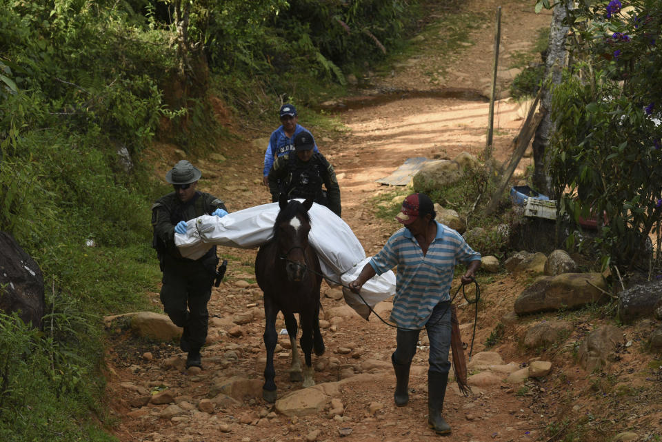 A police officer helps a peasant transport the body of one of at least five people killed during a skirmish between illegal armed groups in Jamundi, southwest Colombia, Friday, Jan. 17, 2020. Authorities say rebels with the former Revolutionary Armed Forces of Colombia operate in the area and may have been involved. (AP Photo/Christian EscobarMora)