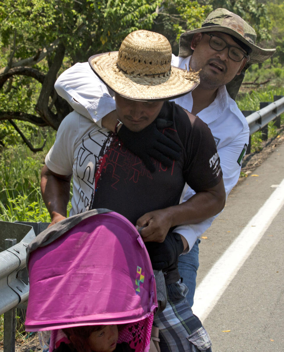 Un migrante centroamericano que empuja un carro con un bebé es detenido por un agente mexicano de inmigración en la autopista a Pijijiapan, en México, el lunes 22 de abril de 2019. (AP Foto/Moisés Castillo)