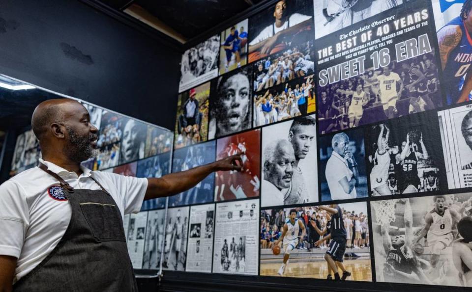 Brian Mack points at wall of The Charlotte Observer art featuring local basketball players at House of Hoops Barbershop in Charlotte, N.C., on Monday, July 1, 2024.