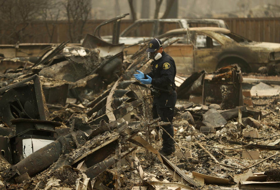 FILE - In this Nov. 15, 2018, file photo, a Sheriff's deputy looks for human remains at a home burned in the Camp fire in Magalia, Calif. Authorities are lifting evacuation orders for some Northern California communities ravaged by the state’s deadliest wildfire but said no traffic will be allowed into the town of Paradise. The Butte County Sheriff’s Office on Sunday said residents of neighborhoods in nearby Magalia can return to the area at noon on Sunday, Dec. 2, and public access will resume 24 hours later. (AP Photo/John Locher, File)