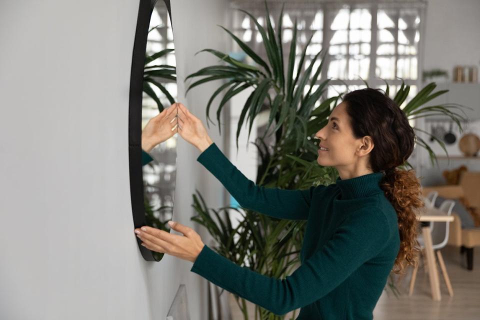 Woman hanging a thick, round mirror on her wall.