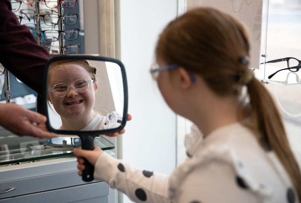 <p>Rosie Johnson, 14, looks in a mirror as she tries on her new glasses at England's first Downs Syndrome eye clinic, at the University of Portsmouth in Hampshire, which has begun offering specialised treatment to people with Down Syndrome, saving them from having to travel to the UK's only other specialist centre in Wales. Picture date: Wednesday May 26, 2021.</p>
