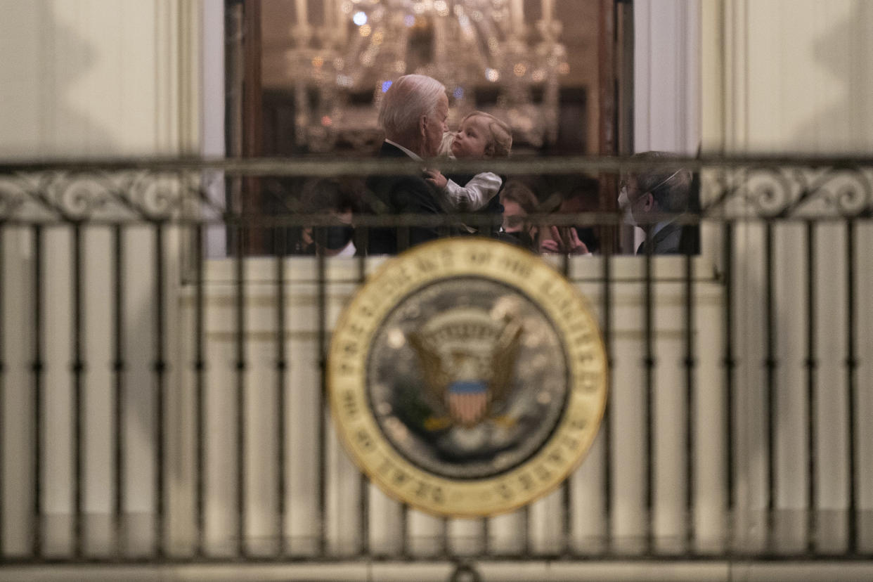 Joe Biden holds a young boy in his arms, as seen through a window of the white house. (Evan Vucci / AP)