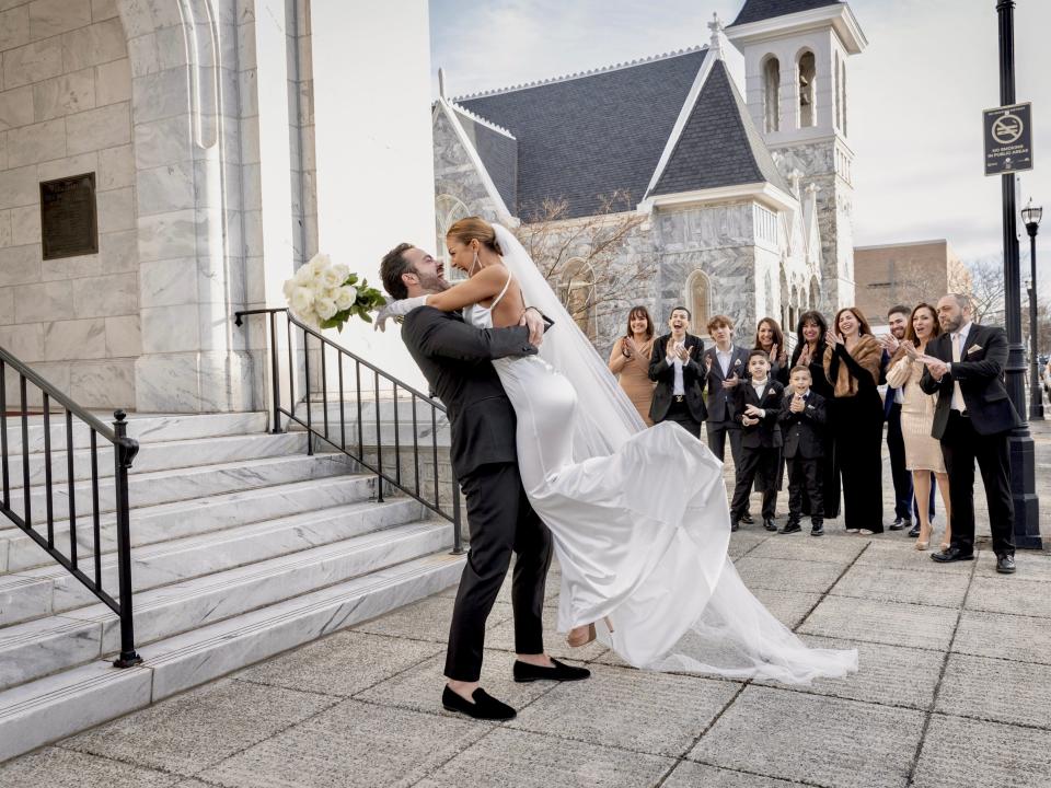 A groom lifting his bride in front of a crowd.