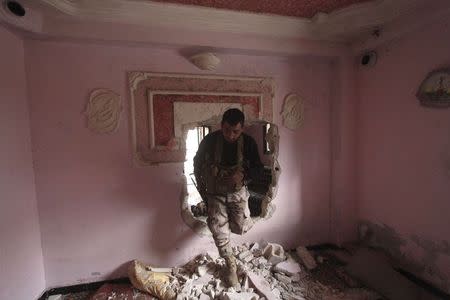 A rebel fighter of al-Jabha al-Shamiya (the Shamiya Front) moves through a hole in a wall inside a house north of Handarat camp in Aleppo, after the group said they took control of the area from forces loyal to Syria's President Bashar al-Assad, February 8, 2015. REUTERS/Hosam Katan
