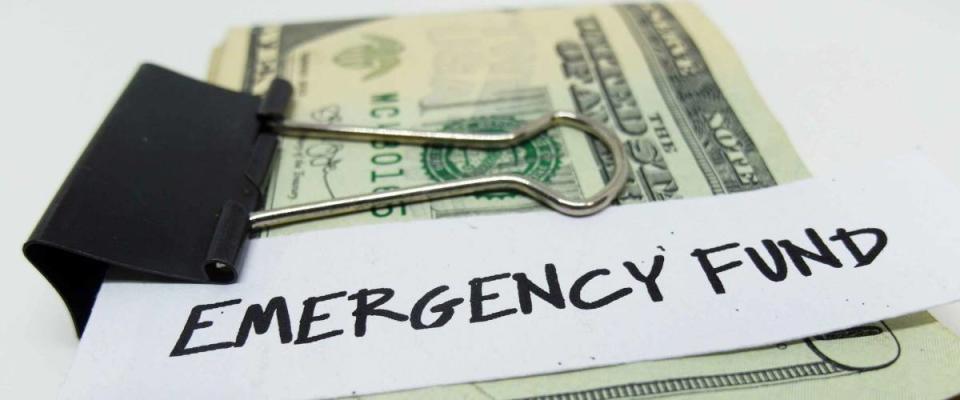 Closeup of US dollars in paper clip on white background with note written EMERGENCY FUND : Concept of setting money saving goal for rainy day.