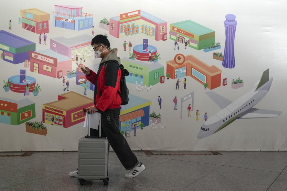 A traveller wearing a face mask with his luggage and passport walks by a poster depicting the Beijing airport on display at the international flight check in counter at the Beijing Capital International Airport in Beijing, Thursday, Dec. 29, 2022. Moves by the U.S., Japan and others to mandate COVID-19 tests for passengers arriving from China reflect global concern that new variants could emerge in its ongoing explosive outbreak — and the government may not inform the rest of the world quickly enough. (AP Photo/Andy Wong)