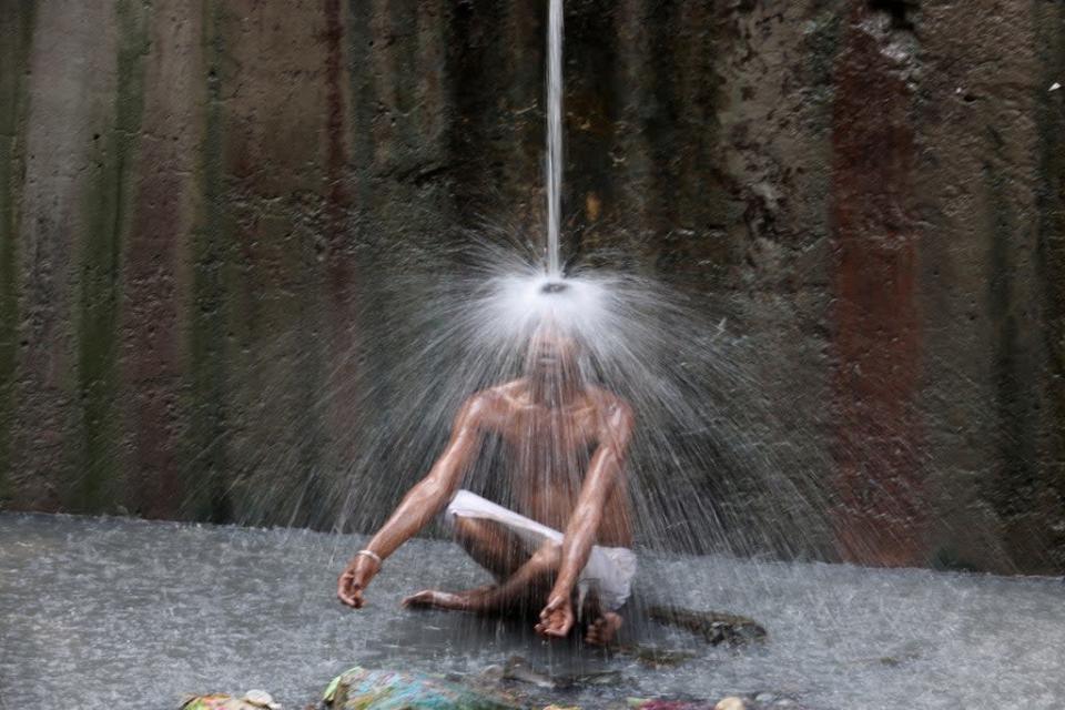 A man cools off under a pipe of flowing water on a hot day in New Delhi, India, on Wednesday   (REUTERS)