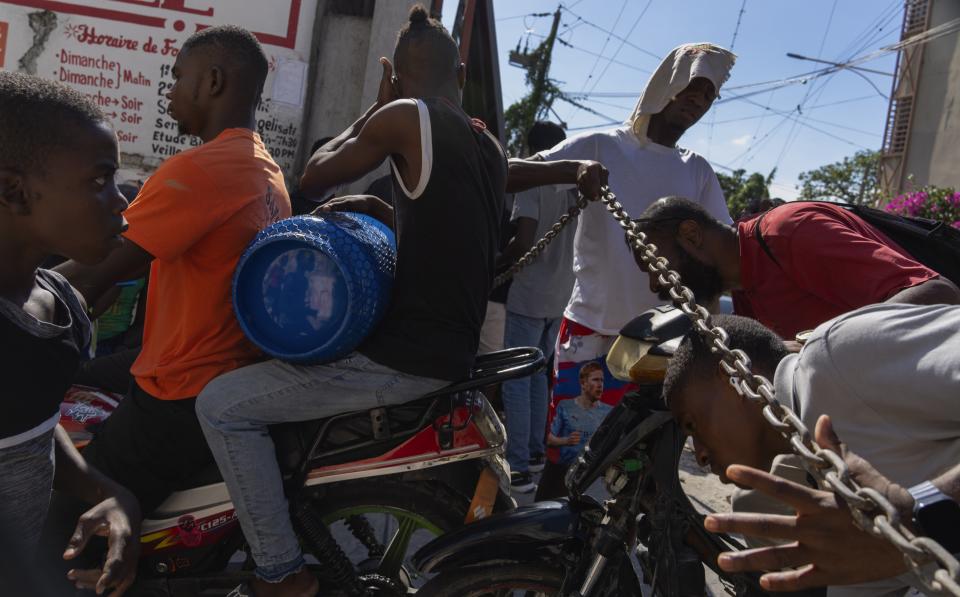 ARCHIVO - Un hombre levanta una cadena utilizada como barricada para que los vecinos pasen al vecindario, mientras preparan una puerta de metal para protegerse de las pandillas en el vecindario de Petion-Ville, Puerto Príncipe, el sábado 20 de abril de 2024. Hace mucho que el sistema de salud de Haití era frágil, pero ahora se acerca al colapso total después de que las pandillas lanzaran ataques coordinados el 29 de febrero contra infraestructura crítica en la capital y otros lugares. (AP Foto/Ramón Espinosa)