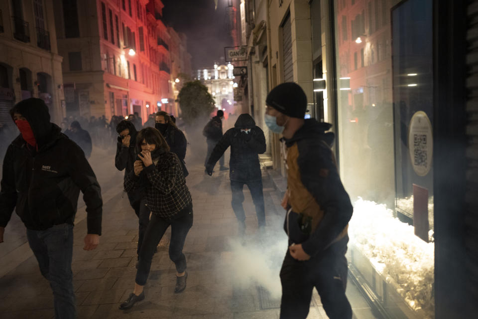 People run from tear gas fired by French riot police during a demonstration in Marseille, southern France, Thursday, March 16, 2023. French President Emmanuel Macron has shunned parliament and imposed a highly unpopular change to the nation's pension system, raising the retirement age from 62 to 64. (AP Photo/Daniel Cole)