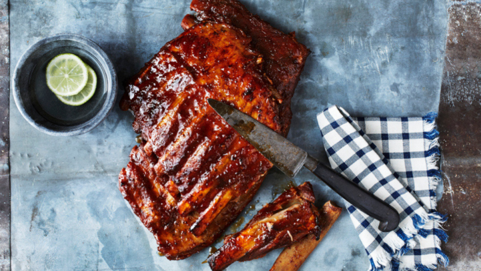 overheard shot of oven-baked baby back ribs with knife on blue background
