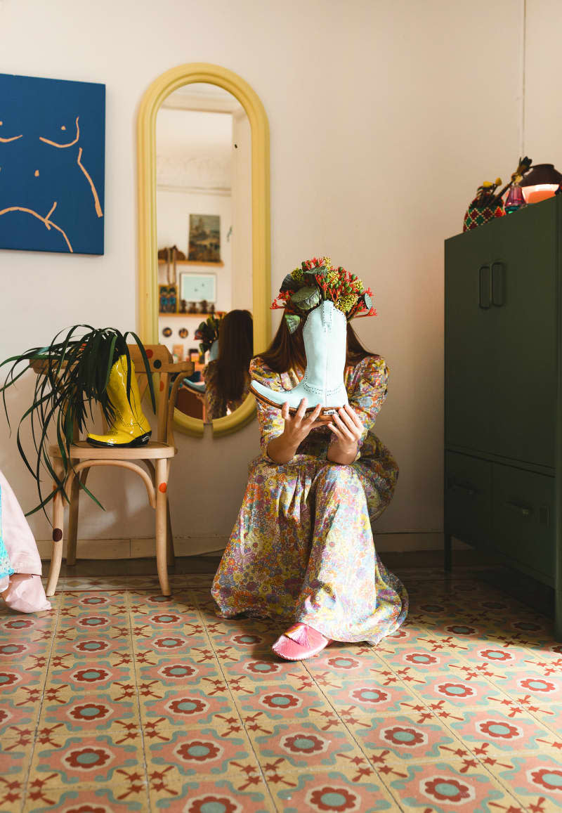 Dweller sits with boots used as vases in bedroom with colorful floor.