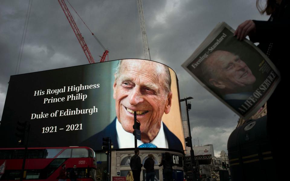 A tribute to Prince Philip shines on Piccadilly Circus whilst a member of public reads a paper with him on the from page - Rick Findler 