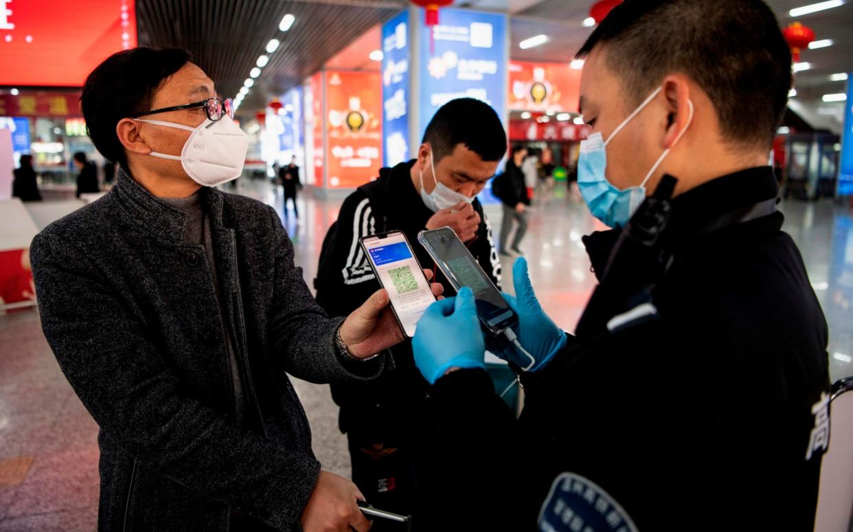 A passenger shows a green QR code on his phone to show his health status to security at Wenzhou railway station - AFP