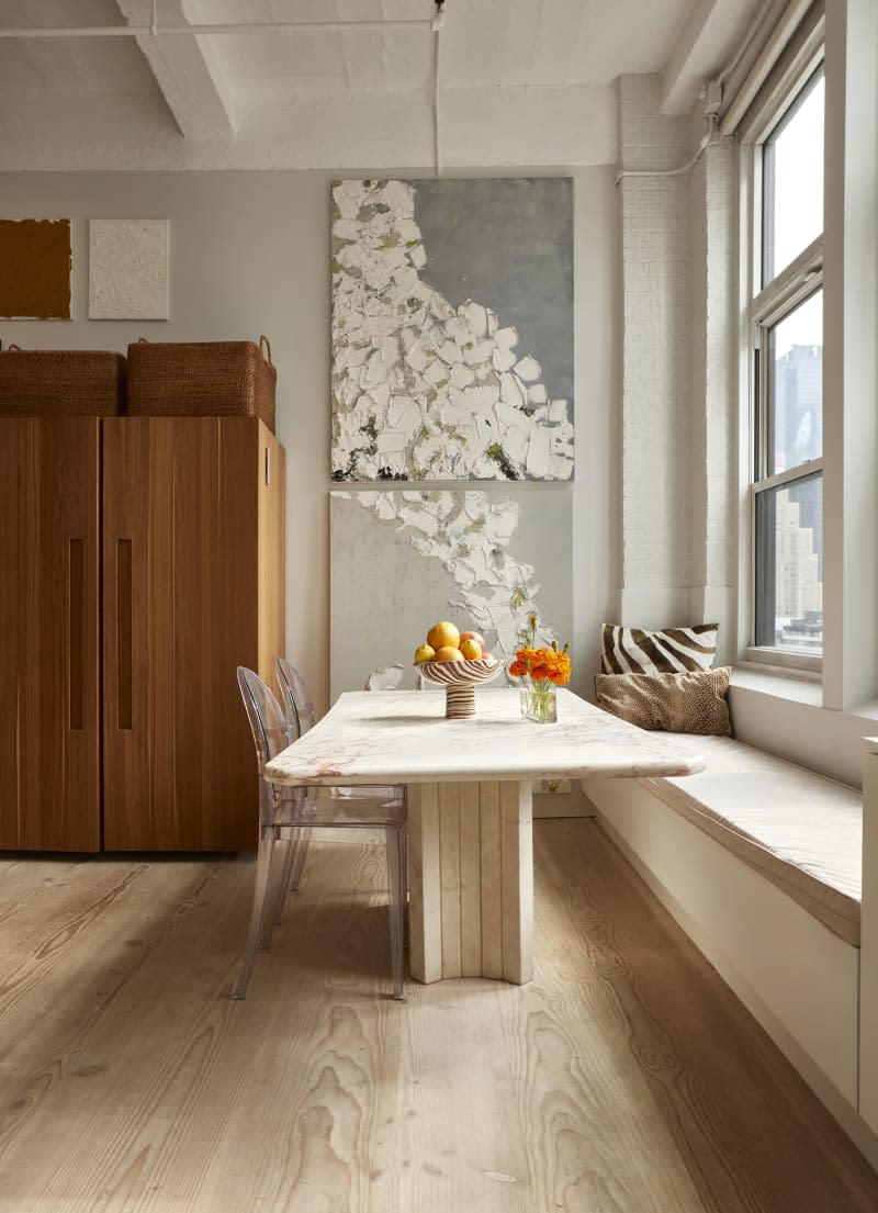 Two art pieces hang above a marble table near a built-in bench