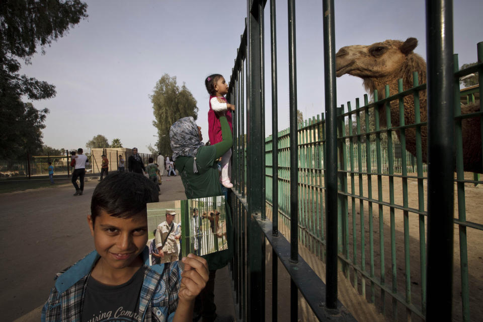 Una mujer sostiene a su hija para que vea a un camello en su espacio del zoo de Bagdad el 15 de marzo de 2013, mientras que Abdullah, de 8 años, posa con una fotografía tomada el 20 de julio de 2003 por Niko Price, de un soldado visitando el entonces recién inaugurado parque. AP Photo/Maya Alleruzzo