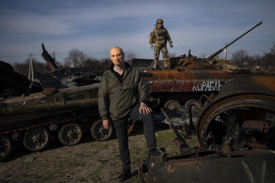 Un civil porta una máscara del presidente ruso Vladimir Putin, a manera de parodia, mientras un soldado ucraniano monta un tanque ruso dañado, el 7 de abril de 2022, en Bucha, en la afueras de Kiev, Ucrania. (AP Foto/Rodrigo Abd)