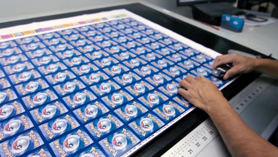 Two hands rest on a sheet of Pokémon cards on a desk