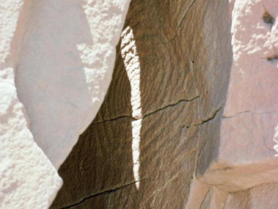 A slice of light cuts through a spiral petroglyph tucked away in sandstone.