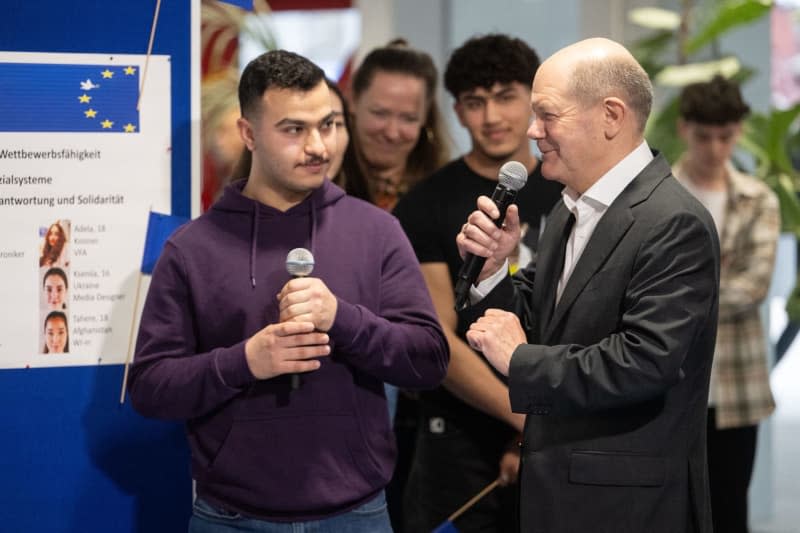 German Chancellor Olaf Scholz (R) talks to pupils during a visit to the Gottlieb Daimler School on the occasion of the EU Project Day at schools. Marijan Murat/dpa