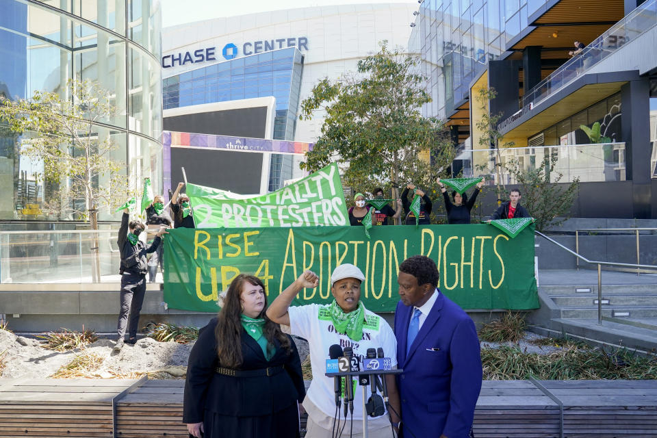 Kareim McKnight, center, talks to reporters during a press conference outside Chase Center, announcing the filing of a federal civil rights lawsuit against the San Francisco Fire and Police Departments in San Francisco, Wednesday, Aug. 10, 2022. McKnight alleges a paramedic, under the orders of a police sergeant, injected her with a sedative while she was handcuffed after protesting the Supreme Court's Roe v. Wade decision during a Golden State Warriors championship game. (AP Photo/Godofredo A. Vásquez)