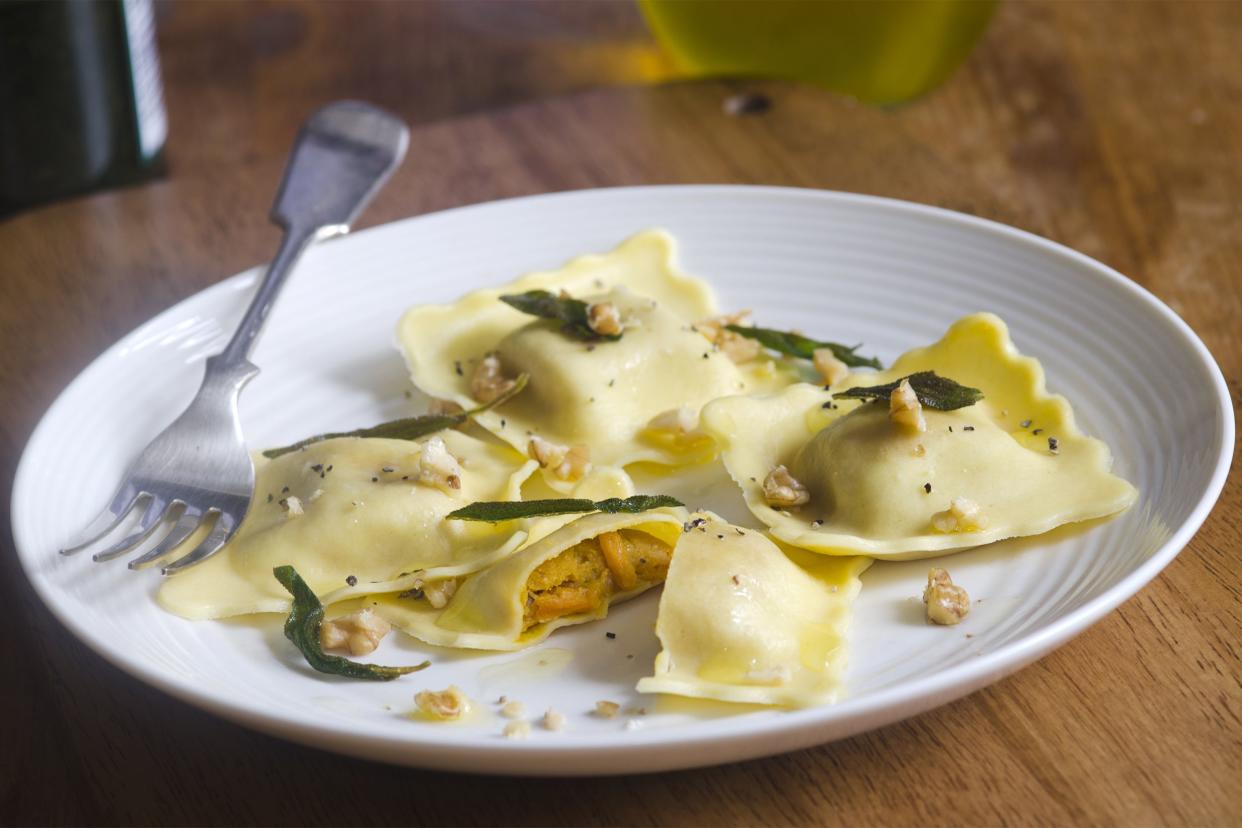 Savory pumpkin ravioli on a white plate with a fork on a wooden table