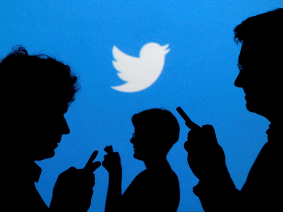 People holding mobile phones are silhouetted against a backdrop projected with the Twitter logo in this illustration picture taken September 27, 2013.