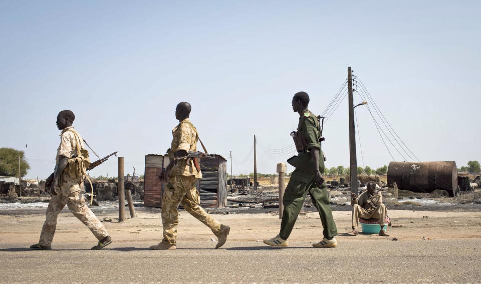 A man, right, sits with his belongings on the side of the road as government soldiers walk past, after government forces on Friday retook from rebel forces the provincial capital of Bentiu, in Unity State, South Sudan Sunday, Jan 12, 2014. On Sunday senior South Sudanese government officers inspected the recaptured town of Bentiu, in northern Unity State, that was the scene of intense fighting between government and rebel forces, while a South Sudanese government official claimed rebels had badly damaged petroleum facilities in the state. (AP Photo/Mackenzie Knowles-Coursin)