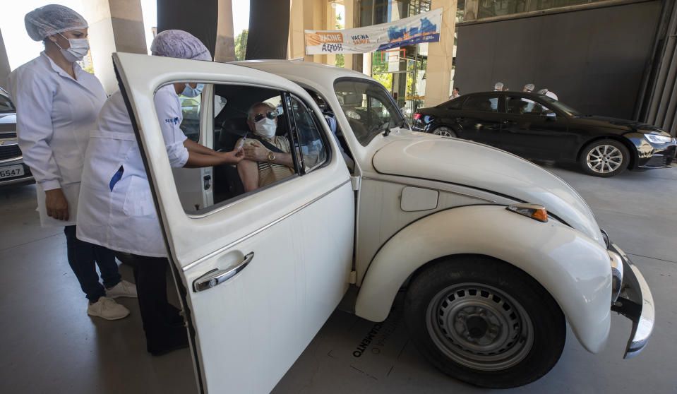 A health worker gives a shot of the Sinovac COVID-19 vaccine to a car passenger during a priority vaccination program for seniors at a drive-thru site set up in the Pacaembu soccer stadium parking lot in Sao Paulo, Brazil, Wednesday, March 3, 2021. (AP Photo/Andre Penner)