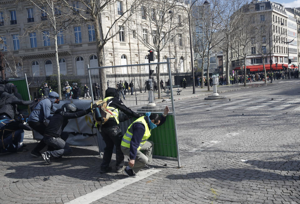 Protesters hide behind street barriers as they clash with police forces during a yellow vests demonstration Saturday, March 16, 2019 in Paris. French yellow vest protesters clashed Saturday with riot police near the Arc de Triomphe as they kicked off their 18th straight weekend of demonstrations against President Emmanuel Macron. (AP Photo/Christophe Ena)