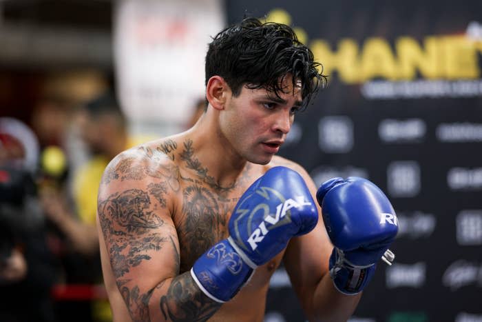 Boxer with gloves in the ring, focused stance, tattooed torso visible