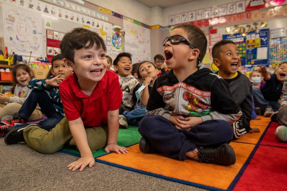 Children seated on a classroom floor smile.