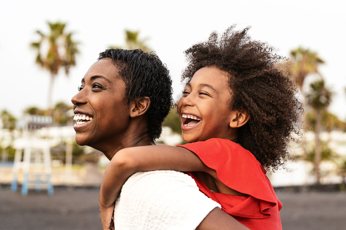 A mother carries her daughter on her back as they explore outside. mother, daughter, family, life insurance